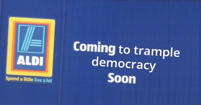 Aldi logo with the phrase 'coming to trample democracy soon' next to it