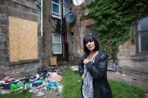 Woman outside boarded-up window with rubbish next to it