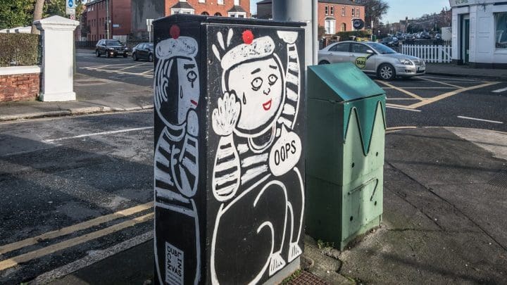 An electrical box by a road, with a mime artist painted on it looking like he's stuck inside
