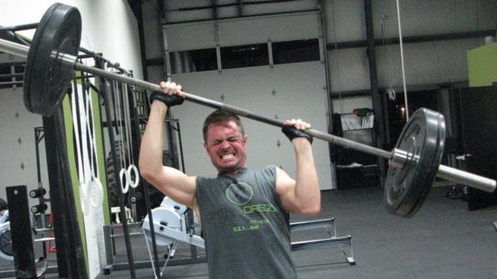 A weightlifter struggling to get both arms straight