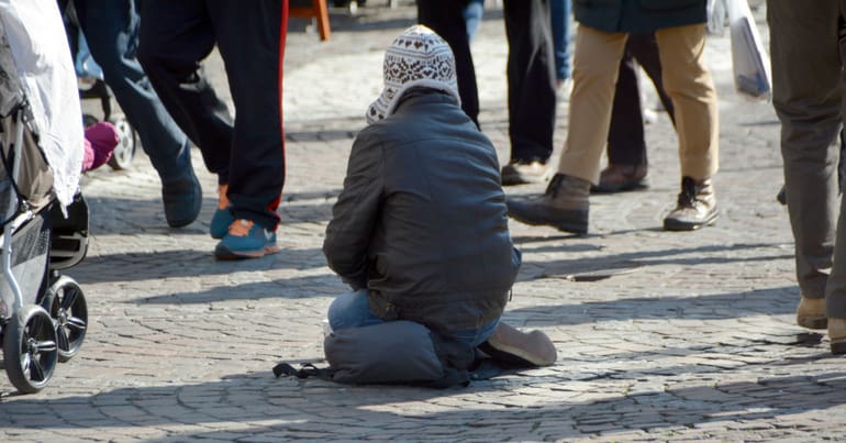 man sitting on pavement as people walk past him