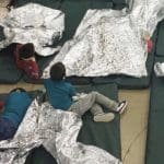 Children on the floor with space blankets in a US detention facility
