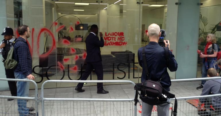 A security guard outside Labour HQ, 'Labour vote no heathrow' sprayed on the window
