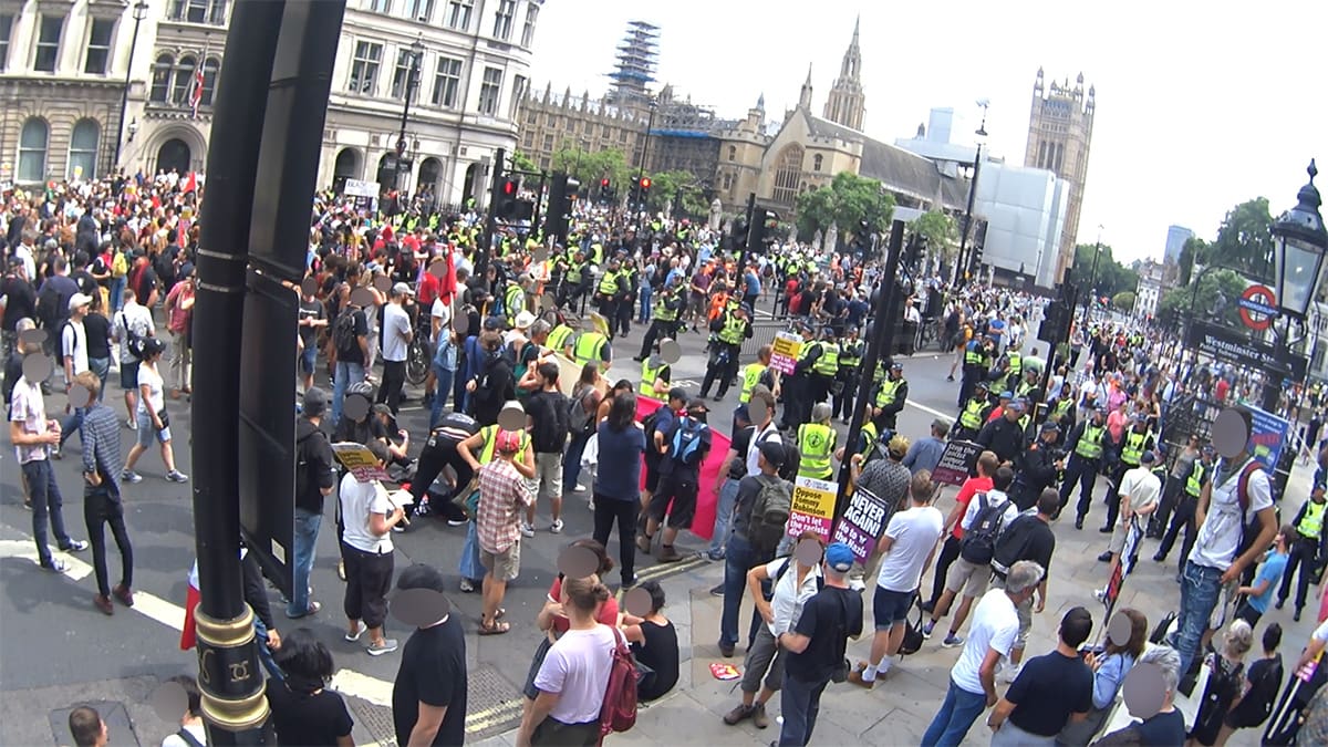 A crowd of anti-fascist protesters watched by lines of police officers