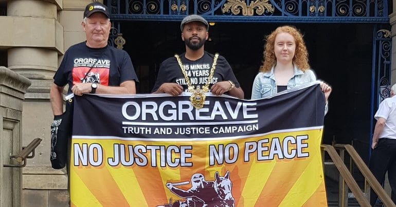 Magid Magid standing behind a 'Truth and Justice for Orgreave' banner