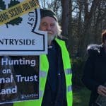 Man holds a placard that says "Stop Hunting on National Trust Land" bTB