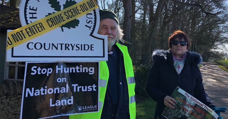 Man holds a placard that says "Stop Hunting on National Trust Land" bTB