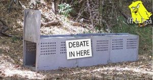 Cage trap with a sign on it that reads 'DEBATE IN HERE'