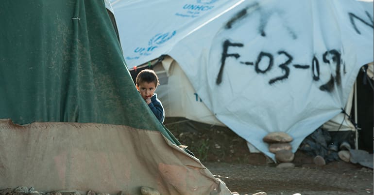 Child looking out from behind tent in UN refugee camp