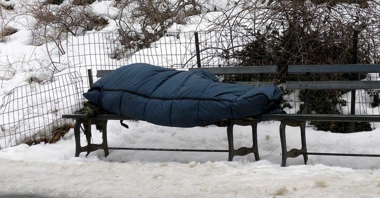 Homeless person sleeping on a bench in the snow