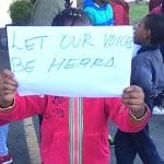 Photo of a child at the protest of asylum seekers in Ireland holding up a sign that says "Let our voices be heard".