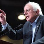 A picture of Bernie Sanders at a lectern pointing at someone or something.