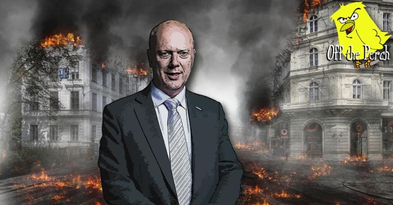 Chris Grayling standing in front of burning buildings