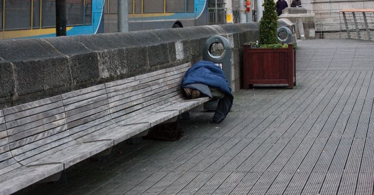 A photo of a homeless man in Dublin sleeping on a public bench.