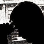 A photo of a sad or depressed person leaning their head against a window while it's raining outside.