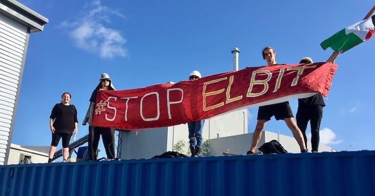 Protestors on top of Elbit roof with banner