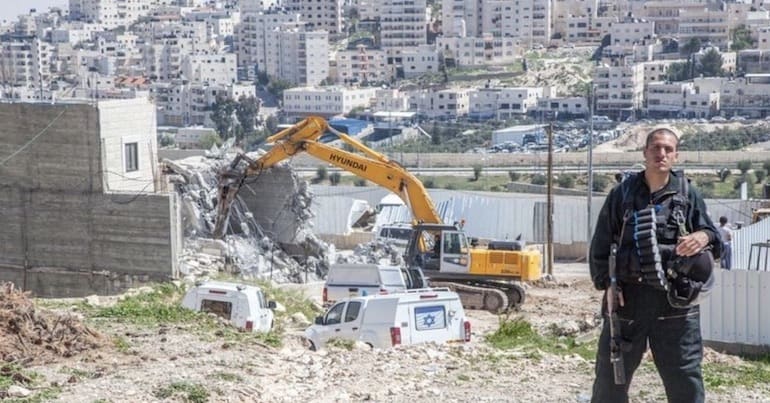 Israeli soldier standing near Palestinian homes under demolition