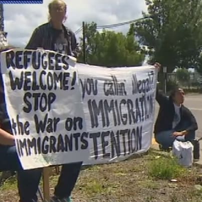 Protesters with sign saying "Refugees welcome. Stop the war on immigrants."