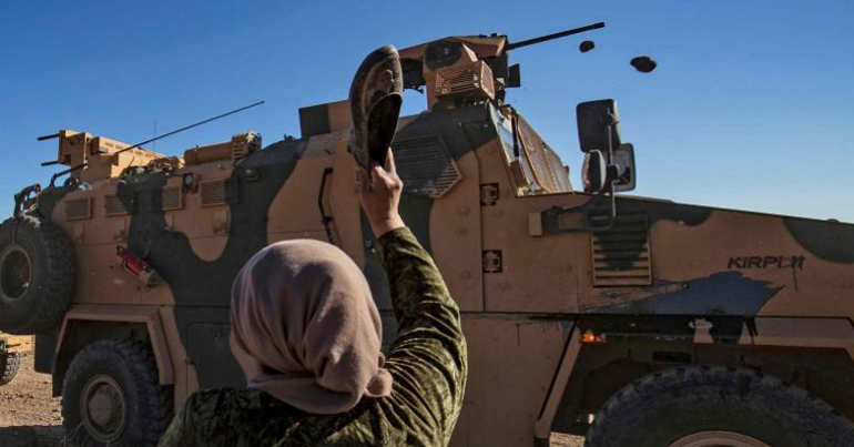 A woman prepares to throw her shoe at a Turkish military vehicle in northeast Syria