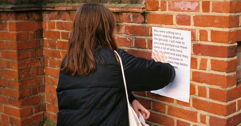 Woman. putting up a Conversations from Calais poster