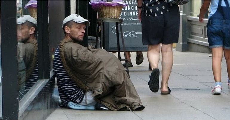 A homeless person sitting on a busy high street pavement