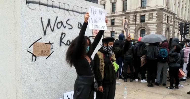 Woman stands in front of Chruchill statue with a sign saying 'the UK is not innocent'