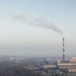 The view of a sparsely populated area with a large industrial chimney emitting smoke