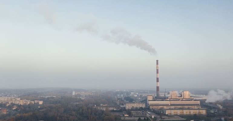 The view of a sparsely populated area with a large industrial chimney emitting smoke