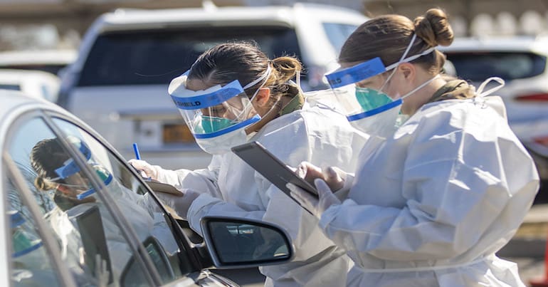 Two people in PPE carry out a coronavirus test in a testing lot