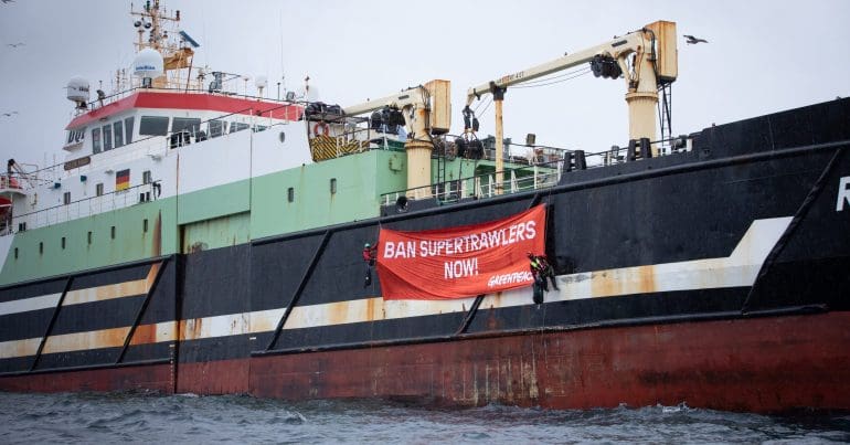 A super trawler with a Greenpeace banner hanging off it that reads: 'BAN SUPERTRAWLERS NOW!'