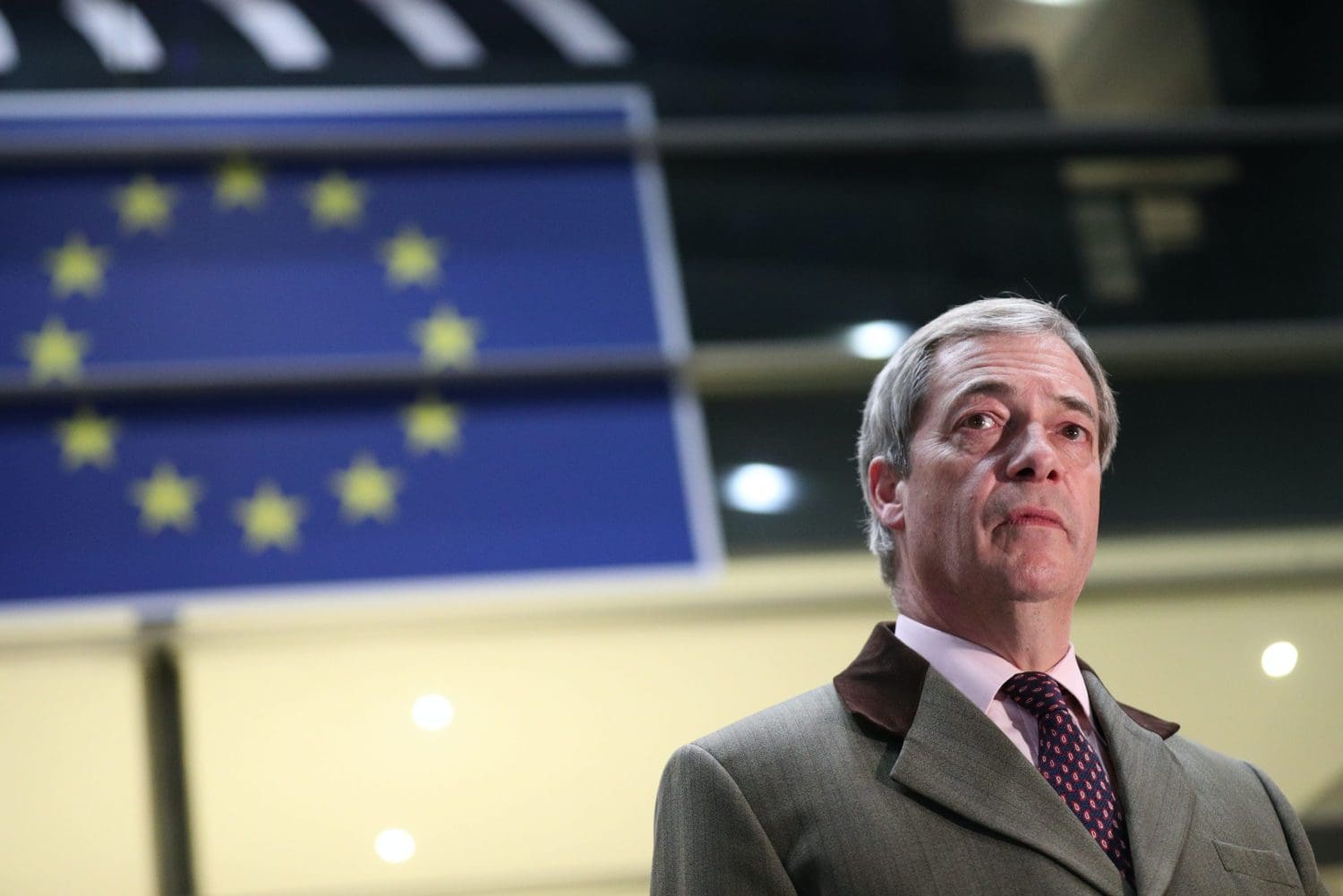 A sad looking Nigel Farage in front of an EU flag