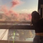 A student protestor looking out at Manchester from an occupied high rise window as coloured flare smoke fills the air