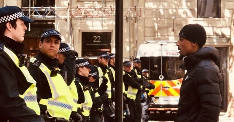 Black Lives Matter protester stands opposite a row of police