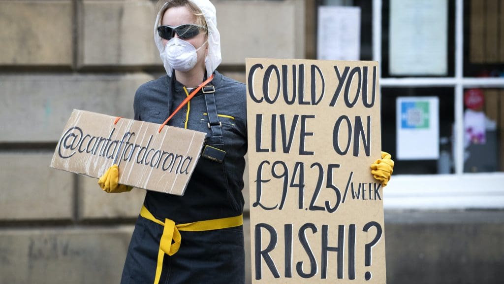A woman holding a placard that reads 'Could you live on £94.25 an hour Rishi'