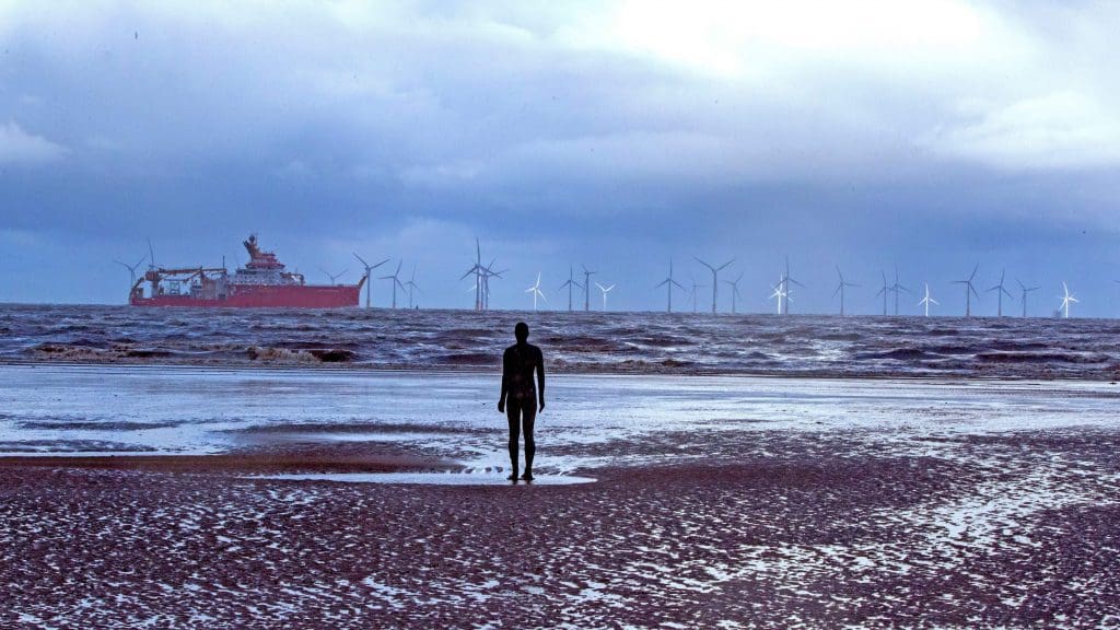 Statue of a man staring out at an offshore windfarm
