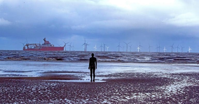 Statue of a man staring out at an offshore windfarm