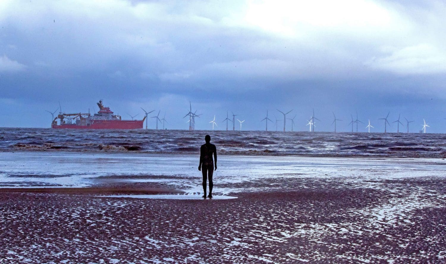 Statue of a man staring out at an offshore windfarm