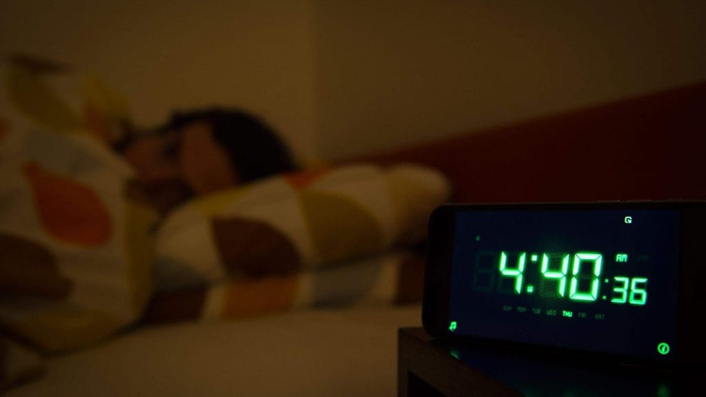 A man in bed with an alarm clock in the foreground