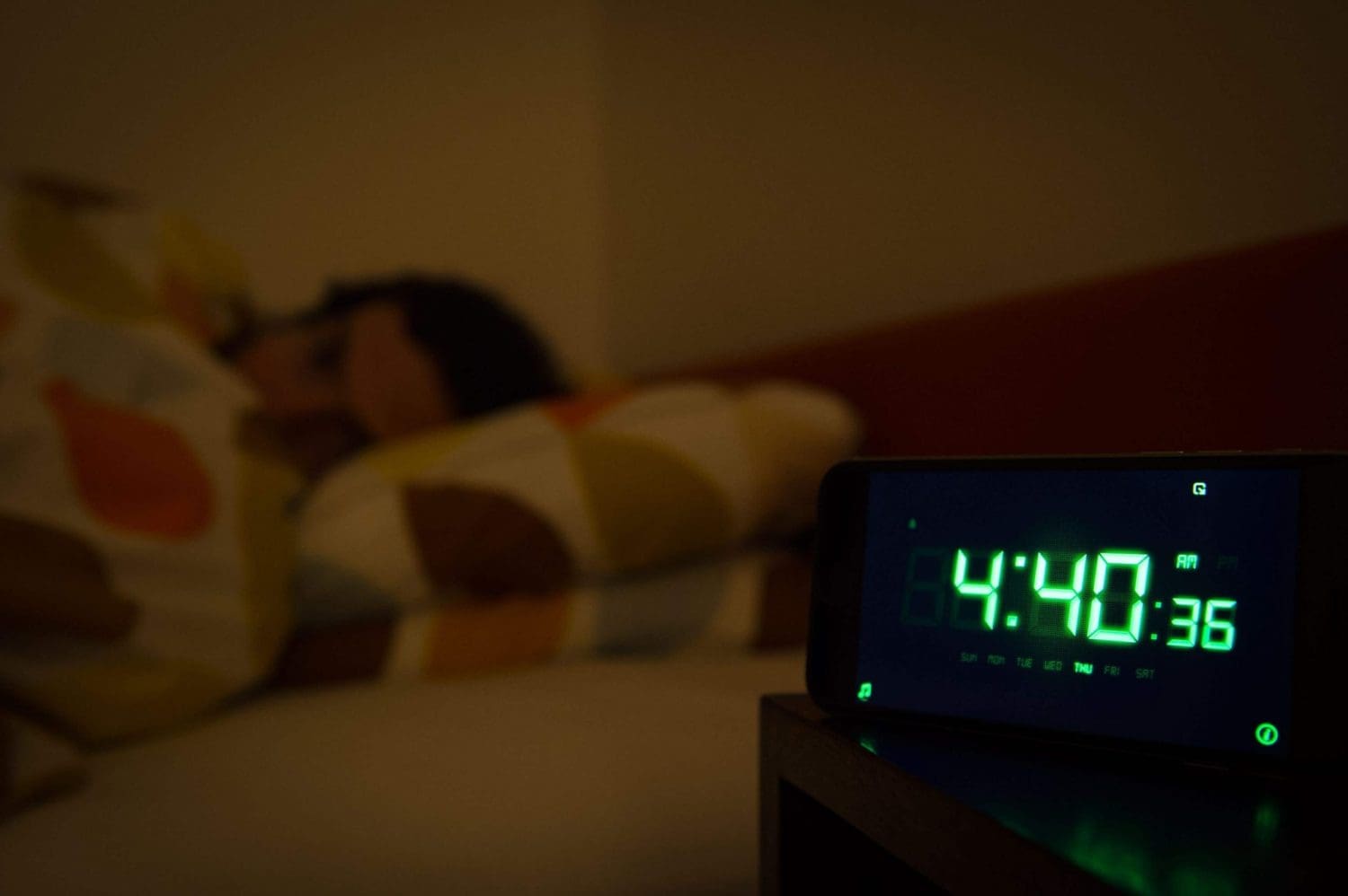 A man in bed with an alarm clock in the foreground