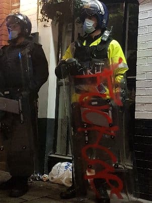 A police officer with a graffitied riot shield outside Bridewell police station