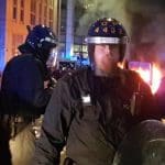 A police line in front of a burning police car