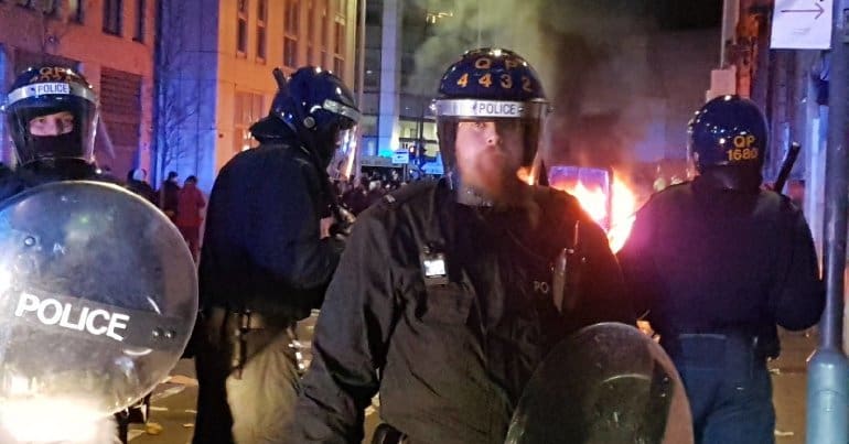 A police line in front of a burning police car