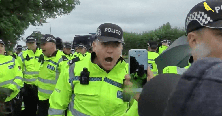 An image of someone using a mobile to film a police officer
