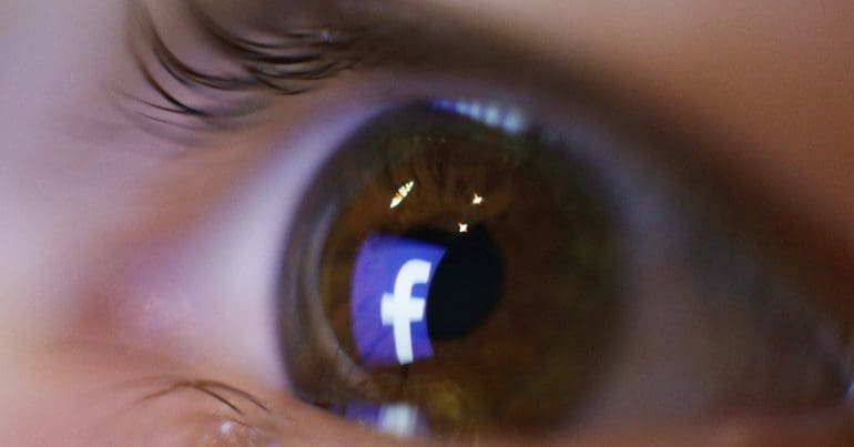 An eyeball with the Facebook logo reflecting in it