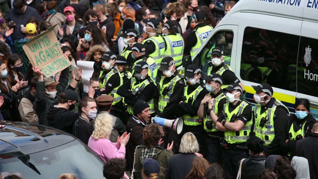 A ring of police officers dwarfed by a crowd of people supporting the men arrested