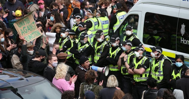 A ring of police officers dwarfed by a crowd of people supporting the men arrested