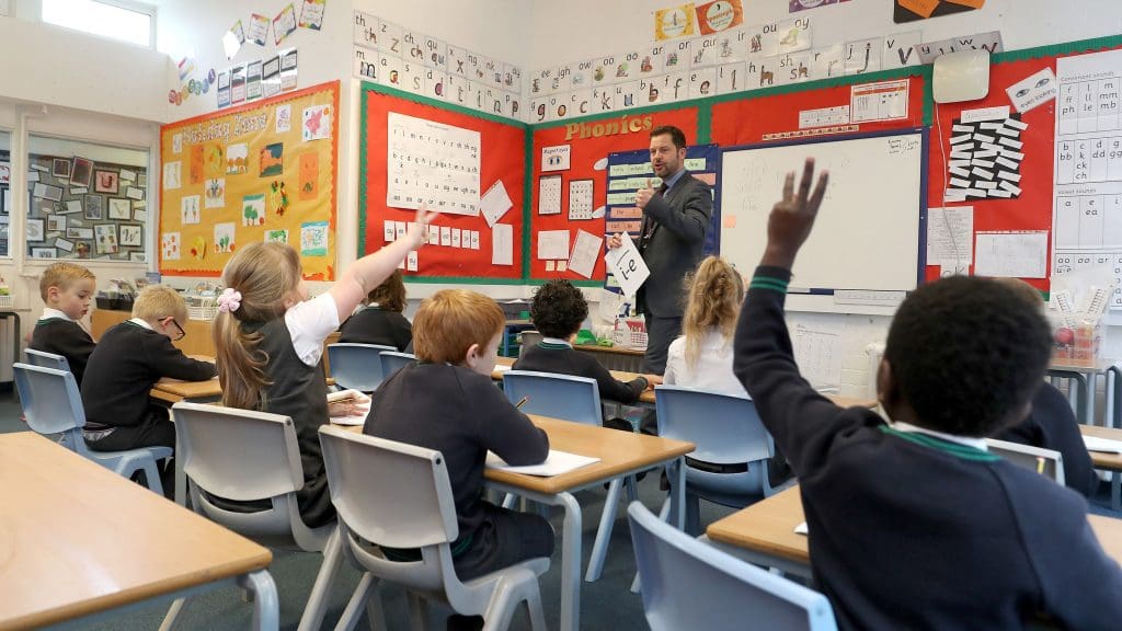 A teacher asking a question and pupils raising their hands