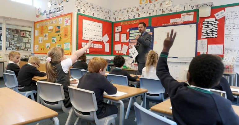 A teacher asking a question and pupils raising their hands