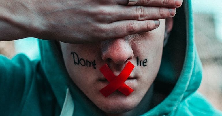Man with had over his eyes and his mouth taped with an X with the words don't lie written on his face