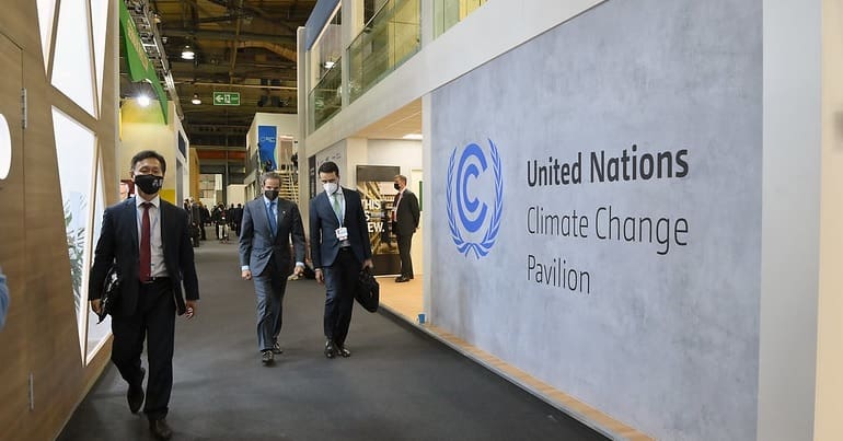 Inside COP26, people in suits walk past the UN Climate Change Pavilion